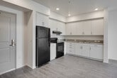 Located at 2222 E First St in Santa Ana, California, this modern single-floor unit offers a thoughtfully designed open-concept layout that seamlessly connects the kitchen and living areas. The kitchen is well-appointed with crisp white cabinetry, ample counter space, a built-in sink, and black appliances including a refrigerator and electric range. Light wood-style flooring extends throughout the main living areas, complementing the clean, bright white walls and recessed lighting that give the space a fresh, contemporary feel. Flush-mount ceiling fixtures provide additional illumination throughout.

The living area is generously proportioned, offering a versatile open space bathed in natural light from large windows that frame outdoor views. The bedroom features plush carpeting and a sliding window that showcases sweeping views of the surrounding hills and landscape, creating a calm and scenic retreat. The full bathroom is equipped with a soaking tub and shower combination, built-in shelving, a single-sink vanity with a large mirror, and wood-style flooring that ties into the rest of the unit's aesthetic. The overall design is clean and modern, with a neutral color palette that creates a bright and welcoming atmosphere throughout.