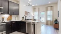 Located in Grand Prairie, TX, this one-bedroom, one-bathroom residence offers a thoughtfully designed single-floor layout that maximizes every square foot. The open-concept kitchen is a standout feature, showcasing rich dark cabinetry with gold hardware, granite countertops, a white subway tile backsplash, and stainless steel appliances including a gas range, built-in microwave, and dishwasher. A central island with an undermount sink and a contemporary multi-arm chandelier overhead adds both function and style to the space. The kitchen flows naturally into the living area, which features light wood-style flooring, tall ceilings, and a glass-paned door that invites abundant natural light and outdoor views. The bedroom offers plush carpeting, generous natural light from large windows, soaring ceilings, and direct access to a walk-in closet with built-in shelving. The bathroom is finished with large-format grey wall tile surrounding a full soaking tub and shower combination, complemented by a granite vanity and matte black fixtures. Light, neutral tones and consistent modern finishes throughout create a cohesive and comfortable ambiance across every room.