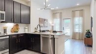 Located in Grand Prairie, TX, this one-bedroom, one-bathroom residence offers a thoughtfully designed single-floor layout that maximizes every square foot. The open-concept kitchen is a standout feature, showcasing rich dark cabinetry with gold hardware, granite countertops, a white subway tile backsplash, and stainless steel appliances including a gas range, built-in microwave, and dishwasher. A central island with an undermount sink and a contemporary multi-arm chandelier overhead adds both function and style to the space. The kitchen flows naturally into the living area, which features light wood-style flooring, tall ceilings, and a glass-paned door that invites abundant natural light and outdoor views. The bedroom offers plush carpeting, generous natural light from large windows, soaring ceilings, and direct access to a walk-in closet with built-in shelving. The bathroom is finished with large-format grey wall tile surrounding a full soaking tub and shower combination, complemented by a granite vanity and matte black fixtures. Light, neutral tones and consistent modern finishes throughout create a cohesive and comfortable ambiance across every room.