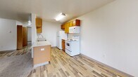 Located in Troutdale, Oregon, this one-bedroom, one-bathroom unit offers a practical and well-organized single-floor layout. The combined living, dining, and kitchen area forms the heart of the home, creating an open, connected space ideal for everyday living. The kitchen is equipped with warm wood-toned cabinetry, a full suite of white appliances including a refrigerator, electric range, built-in microwave, and dishwasher, along with a countertop peninsula that provides additional prep space and separates the kitchen from the living area. Light wood-style vinyl flooring runs throughout the kitchen and entry areas, while plush carpet adds comfort to the living room and bedroom. The bedroom is a well-proportioned retreat featuring a window with views of surrounding greenery and access to a closet. A second closet provides additional storage. The full bathroom includes a single-sink vanity with ample cabinet storage, a toilet, and a bathtub/shower combination with a tile-style floor. A dedicated laundry area adds everyday convenience. Textured ceilings and neutral white walls are consistent throughout. A balcony off the main living area overlooks a lush green lawn and a towering evergreen tree, offering a peaceful outdoor connection to the natural surroundings of the Pacific Northwest.