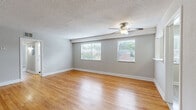Located at 4440 Roanoke Pkwy in Kansas City, MO, this single-floor, three-bedroom, one-bathroom home offers a well-organized and functional layout. The living room serves as the heart of the home, featuring warm hardwood flooring, a ceiling fan with light fixture, textured ceilings, and multiple windows dressed with blinds that invite natural light and views of the surrounding neighborhood. A pass-through opening connects the living area to the kitchen, which is equipped with white cabinetry, stainless steel appliances including a refrigerator and dishwasher, light wood-look flooring, and a window above the counter. The three bedrooms are carpeted for comfort, each featuring a ceiling fan and closet storage. The primary bedroom includes a generously sized walk-in closet with dual hanging rods and shelving. The bathroom features a tiled tub-shower surround with a decorative mosaic accent strip, complemented by a window for natural ventilation. Throughout, neutral gray walls and white trim create a clean, cohesive aesthetic that carries across every room in the home.