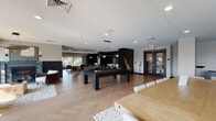 Westley Social in Kansas City, Missouri is a thoughtfully designed communal amenity space that seamlessly blends entertainment, relaxation, and social gathering. The open-plan layout features herringbone-patterned hardwood flooring throughout, unifying the various functional zones with a sense of warmth and cohesion.

The game area serves as a central focal point, anchored by a bold black billiards table and a shuffleboard, offering residents ample space for recreation. Adjacent to it, a fully equipped kitchen impresses with sage-green cabinetry, striking black marble backsplash, a butcher-block island with seating, stainless steel appliances, and pendant lighting — ideal for entertaining and communal cooking.

A dedicated lounge area provides a comfortable retreat, furnished with mid-century-inspired leather chairs, a woven coffee table, and a wall-mounted TV framed by curated artwork. Dark wainscoting adds a sophisticated contrast to the neutral walls. A separate sitting area features a stunning marble-surround fireplace, a circular statement chandelier, and large glass doors opening directly to the outdoor pool deck, flooding the space with natural light and seamless indoor-outdoor connectivity.

The poolside transition zone offers bistro-style seating beside floor-to-ceiling windows overlooking the sun-drenched terrace, complete with pergola and lounge furnishings, rounding out this dynamic and inviting social destination.
