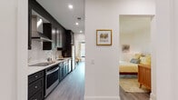This thoughtfully designed single-floor residence at 585 North Ave in New Rochelle, NY offers a cohesive blend of modern finishes and comfortable living spaces. The galley-style kitchen is a standout feature, showcasing dark shaker cabinetry, crisp white quartz countertops, a classic subway tile backsplash, stainless steel appliances, and a deep undermount sink beneath a sleek arc faucet — all complemented by recessed lighting and durable wood-look flooring that flows throughout the home.

The living area is bright and welcoming, with a large bank of windows that frame views of the surrounding neighborhood and fill the room with generous natural light. Stylish patterned drapery adds warmth and character to the space.

The bedroom offers a serene retreat, highlighted by an elegant panel-detailed accent wall that lends architectural interest. The room connects seamlessly to the rest of the home, maintaining the consistent warm and airy aesthetic found throughout.

The bathroom is finished to a high standard, featuring large-format neutral floor tiles, a white vanity with a marble-look countertop, a backlit mirror, and a glass-enclosed shower — creating a clean, spa-like environment. Together, these spaces form a polished, move-in-ready home in a well-located New Rochelle address.