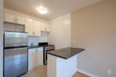 Located at 106 Goodwood Park Crt in Toronto's East End, this well-appointed one-bedroom, one-bathroom unit offers a functional and comfortable layout across a single floor. The living room is generously proportioned, bathed in natural light through large windows that frame views of mature trees, and finished with gleaming parquet hardwood flooring that runs throughout the unit. Radiator heating units beneath the windows underscore the building's classic construction. The open sightline between the living room and kitchen creates an airy, connected feel. The galley-style kitchen is thoughtfully updated with crisp white cabinetry, dark granite countertops, tile flooring, and modern stainless-steel appliances, providing ample storage and workspace. The bedroom offers a comfortable footprint with a built-in sliding-door closet and its own window overlooking the surrounding greenery. The bathroom is clean and bright, featuring a full soaker tub with white tile surround and chrome fixtures. A private balcony extends the living space outdoors, offering a pleasant treetop and cityscape view with lush seasonal foliage. A hallway entry connects all rooms efficiently, completing this practical and inviting urban residence.