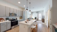 Located at 7488 Universal Blvd in Orlando, Florida, this single-floor residence offers a thoughtfully designed open-concept layout with contemporary finishes throughout. The kitchen serves as the centerpiece, featuring gray shaker-style cabinetry, white quartz countertops, a large island with an undermount sink and bar seating, stainless steel appliances — including a French door refrigerator, electric range, and microwave — as well as a classic subway tile backsplash and warm wood-look flooring. Pendant lighting above the island adds a stylish touch. The kitchen flows seamlessly into the living area, which is bright and inviting, with large windows dressed in layered curtains that allow abundant natural light. The bedrooms are well-appointed, with plush carpeting, generous windows, and distinct accent walls that lend each room its own character. The primary bathroom features dual vanities with gray cabinetry and white countertops, wood-look flooring, and direct access to a spacious walk-in closet outfitted with built-in wire shelving. The overall aesthetic is modern and cohesive, combining neutral tones with carefully chosen accent details for a polished, comfortable living environment.