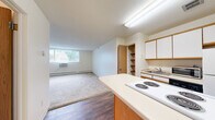 Located at 2210 Skillman Ave E in North St. Paul, Minnesota, this one-bedroom, one-bathroom residence offers a practical and efficient layout across a single floor. The open-concept kitchen anchors the main living area and features a central island with a built-in electric cooktop, white cabinetry with wood-trimmed accents, ample overhead storage, a refrigerator, dishwasher, and a microwave. Rich hardwood-style flooring runs throughout the kitchen and entryway, creating a clean contrast to the plush carpeting found in the living and bedroom areas. An open-shelf storage closet adjacent to the kitchen provides convenient organizational space. The living area is generously sized relative to the overall footprint, bathed in natural light from a large window offering views of the surrounding greenery, and equipped with a baseboard heating system and a wall-mounted air conditioning unit. The spacious primary bedroom continues the neutral, light-filled aesthetic with soft carpet, a wide window, and a baseboard heater. The full bathroom is finished with warm earth-tone tile flooring, a white vanity with under-cabinet storage, a large mirror, and a bright Hollywood-style light bar above. This unit offers a well-organized, comfortable living environment in a quiet North St. Paul neighborhood.