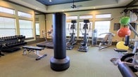 This fitness center offers a comprehensive workout environment designed to accommodate a variety of exercise routines. The space is thoughtfully laid out across a single floor, providing room for both cardio and strength training activities without feeling cramped. A freestanding punching bag serves as a centerpiece, ideal for combat-style conditioning workouts. Surrounding it, the facility features multiple elliptical trainers and at least one treadmill, catering to cardio enthusiasts. A weight bench and additional strength training equipment round out the offerings, ensuring a full-body workout experience. Large windows fitted with adjustable blinds line the walls, flooding the room with natural light while allowing for privacy and glare control. A ceiling fan overhead aids in air circulation, contributing to a comfortable exercise environment. The walls are accented with large mirrors, enhancing the sense of space and allowing users to monitor their form during workouts. Neutral-toned carpeting and warm wall colors give the space an inviting, clean aesthetic. Crown molding and recessed lighting add a polished architectural touch, elevating the overall ambiance of this well-appointed fitness facility.