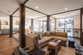 Located at 2124 W Meeker St in Kent, Washington, this single-floor space showcases a thoughtfully designed interior that blends contemporary aesthetics with functional layouts. The open floor plan allows for a seamless flow between distinct areas, unified by warm wood-style flooring and striking geometric patterned tile that anchors the central gathering zones.

The living area is defined by exposed dark structural columns, recessed lighting, and a prominent textured grey brick accent wall that adds an industrial edge to the otherwise modern interior. Large windows allow natural light to fill the space, offering views of the surrounding outdoor patio area through full-height glass and dark-framed doors.

A designated lounge area features a cozy seating arrangement, while a separate nook with built-in display shelving and accent lighting provides an intimate retreat within the open layout. The dining area transitions naturally into the space, complemented by pendant lighting overhead.

The kitchen is a standout feature, outfitted with professional-grade stainless steel appliances including a double oven and range with a bold stainless hood. Sleek grey cabinetry pairs with warm wood floating shelves, under-cabinet lighting, a textured white chevron tile backsplash, and generous countertop workspace, creating a highly functional and visually refined cooking environment.
