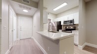 This well-designed single-floor residence offers a clean, modern aesthetic throughout, unified by light wood-style flooring and warm neutral tones on the walls. The open-concept kitchen is a standout feature, boasting white shaker-style cabinetry with brushed nickel hardware, light quartz countertops, and a peninsula with an undermount sink and modern pull-down faucet. A full suite of stainless steel appliances — including a refrigerator, electric range, microwave, and dishwasher — completes the functional and stylish kitchen. Recessed and flush-mounted lighting illuminates both the kitchen and adjacent living area, which offers generous open space and a skylight that brings in additional natural light. A fireplace anchors the living room, adding a warm focal point to the space. The bedroom features vaulted ceilings with a ceiling fan, a large sliding-door closet with vertical blinds, and a window dressed with horizontal blinds that filters in soft natural light. The bathroom connects directly to the bedroom and includes a wide vanity with white cabinetry, quartz countertops, and a full soaking tub. Throughout the residence, consistent finishes and thoughtful details create a cohesive, move-in-ready living environment.