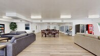Located at 1560 Yosemite Dr in the Eagle Rock neighborhood of Los Angeles, this single-story community facility offers a generous and well-organized layout across one expansive floor. The interior is finished with light wood-look flooring throughout, crisp white walls, and bright fluorescent lighting that creates a clean, welcoming atmosphere.

The living area is divided into two distinct seating zones. One section features plush gray sofas arranged around a flat-screen television flanked by bookshelves, providing a comfortable space for relaxation and entertainment. The adjacent lounge area offers neutral-toned sofas and accent chairs positioned near large windows that invite abundant natural light and views of the surrounding greenery.

A communal dining area accommodates multiple dining tables and dark wood chairs, making it well-suited for group gatherings and meals. The mailroom area includes rows of individual resident mailboxes and additional dining seating, anchored by a central column decorated with hanging floral accents.

The dedicated laundry room is equipped with multiple washing machines and dryers, a folding counter, and a clean, utilitarian layout. Two ADA-compliant bathrooms are outfitted with grab bars, comfort-height fixtures, and light wood-look flooring, ensuring accessibility for all users. The overall design prioritizes functionality, comfort, and community engagement.