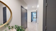 Located in the heart of downtown Indianapolis, this contemporary 2-bedroom, 2-bathroom residence at 220 Meridian offers a thoughtfully designed single-floor layout with high-end finishes throughout. The open-concept kitchen and living area serves as the centerpiece of the space, featuring a large waterfall-edge island with seating, sleek white upper cabinetry paired with warm wood-toned lower cabinets, stainless steel appliances, and a modern linear pendant light fixture. Light hardwood-style flooring flows seamlessly through the main living areas, enhancing the bright, airy atmosphere. The living room is defined by dramatic floor-to-ceiling windows that frame panoramic downtown skyline views and flood the space with natural light. Both bedrooms continue the floor-to-ceiling window theme, offering expansive city views and a serene retreat. The primary bedroom includes a ceiling fan and generous proportions. Each bathroom is finished in a clean, contemporary style with large-format tile, wood-toned vanities, white quartz countertops, and backlit mirrors. A well-proportioned hallway with dark-framed interior doors and recessed lighting connects all rooms, adding to the residence's polished, modern aesthetic.