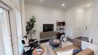 This single-floor residence is thoughtfully designed with a modern aesthetic, blending functionality and style throughout its well-organized layout. The open-concept living area serves as the heart of the unit, featuring dark hardwood-style flooring, recessed lighting, and crisp white walls. A tufted leather sofa, cowhide accent chair, and a round metal coffee table anchor the space, complemented by a wall-mounted media console and a brass-accented open shelving unit. Tall windows dressed with floor-length curtains draw in natural light and connect the interior to the outside.

The kitchen is outfitted with dark espresso cabinetry, a subway tile backsplash, light quartz countertops, and a full suite of stainless steel appliances. An adjacent dining area with a wood table flows seamlessly from the kitchen. A compact built-in desk nook provides a dedicated workspace with a floating shelf above for display and storage.

The primary bedroom features carpet flooring, a ceiling fan, a walk-in closet, and direct access to an en-suite bathroom. A second bedroom offers a large window, ceiling fan, and decorative floating shelves. The bathroom includes a soaking tub with shower, white tile surround, and dark wood vanity with a white countertop.