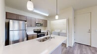 This 1-bedroom, 1-bathroom unit is thoughtfully designed to maximize functionality and comfort across its single floor. Light-toned luxury vinyl plank flooring flows throughout the open-concept living and kitchen areas, complemented by neutral warm-white walls that lend a clean, modern aesthetic.

The kitchen is a standout feature, anchored by a large island with a striking quartz countertop displaying subtle veining. Taupe shaker-style cabinetry offers ample storage, while a full suite of stainless steel appliances — including a refrigerator, electric range, and built-in microwave — provides everything needed for everyday cooking. Pendant lighting above the island adds a polished touch. A dedicated in-unit laundry closet with side-by-side washer and dryer is conveniently accessible from the kitchen area.

The bedroom is a comfortable, carpeted retreat with a window framing views of surrounding greenery, allowing natural light to fill the space. A wall-mounted mini-split unit provides efficient climate control. The bedroom connects to a generous walk-in closet with wire shelving on two walls.

The bathroom features a full tub-shower combination, modern fixtures in brushed nickel, a quartz-topped vanity, and wood-toned cabinetry. Consistent flooring and finishes throughout create a cohesive, move-in-ready living environment.