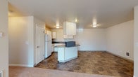 This single-floor unit is thoughtfully laid out to maximize functionality across its living spaces. The kitchen serves as a central hub, featuring white cabinetry with light wood trim, dark laminate countertops, and a peninsula that provides additional prep space and separates the kitchen from the adjoining living area. Tile flooring in a stone-like pattern runs throughout the kitchen and extends into the main living space, offering both durability and visual continuity. A full suite of appliances, including a white refrigerator and dishwasher, is integrated into the kitchen alongside a double-basin sink set beneath upper cabinetry.

The living area is generously sized, transitioning from tile to plush carpeting, and is equipped with a ceiling fan with light fixture. A sliding glass door with vertical blinds opens to an outdoor patio, allowing natural light to filter into the space. The bedrooms are carpeted and feature baseboard heating units, windows with blinds for natural light and privacy, and neutral wall tones throughout.

The bathrooms are finished with stone-patterned tile flooring, white vanities, and full tub-shower combinations with curved curtain rods, maintaining a clean and practical aesthetic consistent with the rest of the unit.