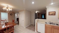 Located at 405 Morrison Ave in Muncie, Indiana, this single-floor home offers a practical and well-organized layout designed for comfortable everyday living. The interior is finished in warm, neutral tones throughout, creating a cohesive and inviting atmosphere from room to room. The kitchen area features white cabinetry, a dishwasher, and a raised countertop that serves as a natural divider between the kitchen and the adjacent dining space, which is accented by light tile flooring and a wooden dining set. Crown molding along the ceilings adds a refined architectural detail that elevates the overall character of the interior. Recessed lighting provides clean, even illumination throughout the main areas. Carpeted flooring transitions seamlessly into the connecting hallway and living spaces, offering a softer feel underfoot. Multiple doorways lead to additional rooms, including what appears to be a comfortable living area visible in the background. A window allows natural light to filter into the space, contributing to the bright and airy feel of the home. The overall layout is efficient and well-connected, making this a welcoming and move-in-ready residence in a residential Muncie neighborhood.