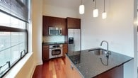This single-floor residence offers a thoughtfully designed layout with a clean, modern aesthetic throughout. The open living and entry area makes an immediate impression with gleaming rich-toned hardwood flooring and crisp white walls that create a bright, airy atmosphere. Multiple large windows dressed with dark blinds invite generous natural light while offering privacy, adding to the sense of openness across the living spaces.

The kitchen is a standout feature, showcasing warm wood cabinetry paired with dark granite countertops and a full suite of stainless steel appliances, including a side-by-side refrigerator with ice maker, wall oven, built-in microwave, and cooktop. A kitchen island with an undermount sink and pendant lighting overhead adds both functionality and style, making it an ideal space for cooking and entertaining.

The bedrooms are finished with soft neutral carpet and feature ample closet space, including a built-in shelving system for organized storage. One bedroom benefits from a bank of large windows, filling the room with natural light.

The bathroom is elegantly appointed with marble-look tile flooring, a marble-topped vanity with an undermount sink, and a full tub-shower combination clad in large-format white tile. Polished chrome fixtures and a large vanity mirror complete the refined, spa-like feel of the space.