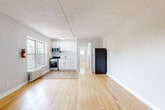 Located on John F. Kennedy Blvd E in North Bergen, NJ, this one-bedroom, one-bathroom unit offers a practical and well-organized layout across a single floor. Light-toned hardwood flooring runs throughout the main living areas, lending warmth and continuity to the space. The open-plan living, dining, and kitchen area forms the heart of the unit, featuring white cabinetry, stainless steel appliances including a gas range and microwave, and a window that brings in natural light. A full-size refrigerator anchors the kitchen area, while the adjacent living and dining space provides room for both relaxing and entertaining. A hallway connects the main living area to the private bedroom, which is a comfortable size and includes a window fitted with an air conditioning unit. The bedroom benefits from access to multiple closets — four in total throughout the unit — offering generous storage. The bathroom is finished with marble-look tile flooring, classic cream wall tiles, a full bathtub, a radiator, and a window for ventilation. The entrance hallway features a utility access panel and track lighting. Overall, the unit presents a clean, neutral palette with functional amenities suited for everyday living.