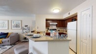 This single-floor residence offers a thoughtfully designed layout that balances comfort and functionality. The open-concept living area is warm and inviting, featuring carpet flooring, a ceiling fan with light fixture, and a textured ceiling. Large windows allow natural light to fill the space, creating a bright and airy atmosphere. The living area flows seamlessly into a dedicated dining space, making it ideal for everyday living and entertaining.

The kitchen is well-equipped and efficient, showcasing rich dark wood cabinetry, tile backsplash, light countertops, and tile flooring. It features a white appliance suite including a refrigerator, electric range, and dishwasher. A peninsula counter with seating provides an additional casual dining option while maintaining an open connection to the rest of the living space.

The bedrooms are generously sized, each featuring soft carpet flooring, ceiling fans, and windows with blinds that offer natural light and privacy. The neutral, warm-toned walls contribute to a calm and restful ambiance throughout.

The bathroom is clean and practical, finished with tile flooring, and includes a louvered door that leads to a walk-in closet area with wire shelving for organized storage. Overall, this residence presents a cohesive, comfortable living environment with functional spaces throughout.