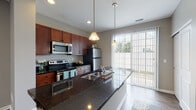Located at 6108 Chestnut Ridge Dr in Columbus, Ohio, this two-story home offers a well-designed layout with modern finishes throughout. The main level features hardwood-style flooring that flows through the open living areas, anchored by a striking kitchen equipped with rich cherry wood cabinetry, dark granite countertops, stainless steel appliances including a range, microwave, and refrigerator, and a large peninsula with a stainless steel sink. Pendant lighting illuminates the kitchen, while a sliding glass door bathes the space in natural light and provides outdoor access. A convenient half bath and an in-unit laundry area with a stacked washer and dryer are also located on the main floor. A white-railed staircase leads to the upper level, where plush carpeted bedrooms offer a comfortable retreat. Each bedroom is finished with neutral gray walls and windows that allow for ample natural light. The upper hallway connects the bedrooms with easy access to shared spaces. Throughout the home, neutral gray walls, white trim, and consistent finishes create a clean, cohesive aesthetic that is both modern and welcoming.