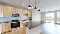 This 1-bedroom, 1-bathroom unit in Monona, Wisconsin offers a thoughtfully designed layout with modern finishes throughout. The open-concept kitchen is a standout feature, boasting light maple cabinetry, dark granite countertops, a classic white subway tile backsplash, stainless steel appliances including a French door refrigerator, electric range, microwave, and dishwasher, as well as a central island with pendant lighting overhead. Wood-look flooring flows consistently throughout the entire unit, lending warmth and visual continuity. The living area is bright and airy, highlighted by sliding glass doors that open onto a private balcony with outdoor views. The bedroom is a comfortable size, featuring a large window that invites natural light and views of the surrounding greenery. A distinctive set of sliding barn doors connects the bedroom to the hallway, adding a contemporary architectural detail. The bathroom is well-equipped with light maple cabinetry, dark granite countertops, a wide vanity mirror with overhead lighting, built-in shelving, and a full tub-shower combination. Clean, neutral wall tones and consistent wood-look flooring create a cohesive and modern aesthetic throughout the space.