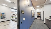 Located at 2924 Snelling Ave N in Roseville, Minnesota, this thoughtfully designed single-floor amenity space offers a generous footprint across three distinct areas. The hallway serves as a polished transition corridor, featuring bold blue accent walls, elegant wall sconces, framed artwork, and keycard-access entry to the exercise room — setting a contemporary tone throughout.

The exercise room is well-equipped for a comprehensive workout experience. Large floor-to-ceiling windows flood the space with natural light and provide outdoor views, while light-toned plank-style flooring adds a clean aesthetic. The room includes multiple treadmills, a multi-station cable machine, a dumbbell rack with weight bench, exercise balls, resistance bands, and medicine ball storage — accommodating a wide range of fitness activities.

The kitchen and lounge area is a standout communal space, designed for both casual gatherings and productive work. The kitchen features granite countertops, stainless steel appliances including a full-size refrigerator and range with a ventilation hood, and ample cabinetry. Adjacent to the kitchen, the lounge offers varied seating arrangements — from bar-height stools to upholstered sofas and private booth-style seating — all bathed in natural light through expansive windows overlooking the outdoors. Coffered ceiling details and designer lighting complete the refined, modern ambiance.