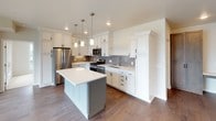 This single-floor residence showcases a thoughtfully designed layout with consistent, high-quality finishes throughout. The kitchen serves as a central highlight, featuring white raised-panel cabinetry with black hardware, a gray subway tile backsplash, stainless steel appliances including a French door refrigerator, gas range, built-in microwave, and dishwasher. A two-toned island with a crisp white quartz countertop provides additional prep space and seating, while pendant lighting and recessed fixtures illuminate the area warmly. Hardwood flooring flows through the kitchen and living areas, adding warmth and cohesion.

The bedrooms are bright and airy, benefiting from large windows that frame verdant outdoor views. One bedroom features direct balcony access, carpet flooring, and generous closet space. Neutral tones throughout create a calm, inviting atmosphere.

Two bathrooms offer distinct yet complementary designs. One features dark slate-toned large-format tile, a gray vanity with white countertop, and a well-lit mirror. The second includes dark linear tile flooring, a light blue vanity, white countertops, and a full tub-shower combination. Both bathrooms are finished with brushed nickel fixtures, maintaining a cohesive and modern aesthetic across the entire residence.