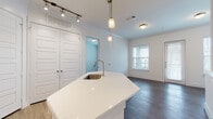 Located at 764 Westinghouse Rd in Georgetown, TX, this single-story residence showcases a clean, contemporary design with consistent finishes throughout. Dark hardwood-style flooring runs throughout the home, providing a warm contrast against the crisp white walls and trim.

The kitchen serves as a central highlight, featuring a large angled island with white quartz countertops and an undermount stainless steel sink with a modern pull-down faucet. A full suite of stainless steel appliances, including a refrigerator, electric range, microwave, and dishwasher, complements the gray cabinetry with a white tile backsplash. Pendant lighting with globe-style fixtures and a track lighting system illuminate the space effectively, enhancing the kitchen's functional and aesthetic appeal.

Adjacent to the kitchen, a spacious living area receives natural light through a window fitted with horizontal blinds. The bedroom is bright and well-proportioned, also featuring a window with blinds that allows ample daylight to filter in.

The bathroom is finished in a modern style with gray cabinetry, a white vanity top, and direct access to a walk-in closet with built-in shelving. The overall layout is efficient and open, offering a cohesive, move-in-ready living environment.