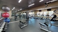 Located at 6400 Bell St in Amarillo, Texas, this fitness center offers a comprehensive, single-floor workout facility designed to support a wide range of exercise routines. The space is thoughtfully laid out to accommodate both cardio and strength training, with clearly defined zones for each type of activity.

The cardio area features multiple treadmills, elliptical machines, and a stationary bike, all positioned in front of large windows that allow natural light to fill the room and provide views of the surrounding outdoor greenery. Wall-mounted televisions are positioned overhead for entertainment during workouts.

The strength training section is outfitted with cable machines and weight benches, supported by full-length mirrors along the walls that enhance the sense of space and allow users to monitor their form. A dedicated free weights area includes a comprehensive dumbbell rack with a wide range of weights, medicine balls, and an assortment of stability and exercise balls neatly stored on racks.

Throughout the facility, dark rubberized flooring provides both durability and safety. Recessed and overhead fluorescent lighting ensures bright, even illumination across the entire space. The neutral-toned walls and mirrored surfaces create an open, functional ambiance well-suited for focused fitness activity.