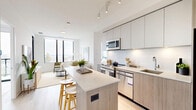 Unit 615 at 500 Upper Wellington Street is a thoughtfully designed three-bedroom, two-bathroom residence located in Hamilton, Ontario. Despite its compact footprint, the unit maximizes every square foot through an efficient single-floor layout and contemporary design choices throughout.

The open-concept kitchen and living area serves as the heart of the unit. The kitchen features two-tone cabinetry combining light wood and white finishes, stainless steel appliances including a full-size refrigerator, built-in dishwasher, and microwave, complemented by a quartz countertop island with bar seating. Light hardwood flooring runs throughout, enhancing the bright, airy atmosphere.

The living area benefits from large black-framed windows that frame sweeping views of the surrounding Hamilton cityscape, and a glass door provides access to an outdoor balcony. The three bedrooms are bright and minimalist, each featuring large windows with panoramic views. The primary bedroom offers a comfortable layout with direct sightlines to the kitchen.

Both bathrooms are finished in a clean, modern style with wood-tone vanity cabinetry, tile flooring, and crisp white walls. The overall aesthetic throughout the unit is cohesive — neutral tones, natural light, and contemporary fixtures create a polished, move-in-ready environment.
