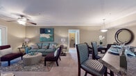 This single-floor residence offers a thoughtfully designed layout that balances comfort and functionality across its main living areas. The open-concept living and dining space forms the heart of the home, where carpet flooring, crown molding, and neutral taupe walls create a cohesive backdrop. The living room features a ceiling fan with light fixture and French doors that open to an outdoor area, allowing natural light to fill the space. An adjacent dining area is defined by a pendant light fixture and chair rail molding, providing an intimate setting for meals.

The galley-style kitchen is outfitted with white cabinetry, dark granite-style countertops, tile flooring, and black appliances, including a range, microwave, and refrigerator. A hallway leads from the kitchen toward additional storage and utility areas.

Both bedrooms are generously proportioned, each featuring plush carpet, ceiling fans, and windows with natural light. One bedroom includes a walk-in closet with built-in shelving. The two full bathrooms mirror each other in finish, each offering white vanity cabinetry, dark countertops, tile flooring, and a shower-tub combination.