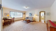 This single-floor residence offers a thoughtfully organized layout that maximizes comfort and functionality. The living room serves as the heart of the space, featuring wall-to-wall carpeting, a large multi-pane window that invites natural light, and a charming arched doorway that adds architectural character. A baseboard heating system runs along the walls, and the room provides ample space for relaxed seating arrangements.

The dining area is open and carpeted, situated adjacent to the kitchen and accented by a window that brings in additional natural light. A built-in white storage cabinet adds practical utility to this area. The kitchen is compact yet well-equipped, featuring white cabinetry, open shelving, a double-basin stainless steel sink, laminate countertops, and a freestanding electric range — all set on easy-care flooring.

The bedroom is a quietly comfortable retreat with carpeted floors, a window with sheer curtains, and warm, understated wall tones that create a restful atmosphere. The full bathroom is finished with large-format tile flooring, a pedestal sink, a toilet, and a soaking bathtub, with a window providing natural ventilation. The overall aesthetic of the space is warm and neutral, with cream-toned walls throughout lending a cohesive, inviting character to every room.