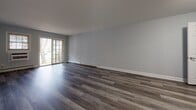 This single-floor residence in Woodbury, NY offers a thoughtfully updated interior with a cohesive, contemporary aesthetic throughout. The living areas are finished with rich, gray-toned hardwood-style flooring that extends across the open layout, complemented by cool gray walls and clean white baseboards. Sliding glass doors and large windows allow natural light to fill the space, creating a bright and airy atmosphere.

The kitchen is well-equipped with white shaker-style cabinetry, including glass-front upper cabinets, granite countertops, a gray tile backsplash, and stainless steel appliances including a gas range, dishwasher, and over-the-range microwave. A dedicated laundry area with a stacked washer and dryer unit is conveniently integrated into the layout.

The bedrooms feature plush carpeting and multiple windows that bring in ample natural light, with wall-unit air conditioning and baseboard heating ensuring year-round comfort. Each bedroom includes closet space for storage.

Two bathrooms serve the residence. The full bathroom features white subway tile surrounding a soaking tub, a white vanity with a marble-style countertop, and light tile flooring. The second bathroom offers a similarly styled vanity with brushed nickel fixtures and a mirrored medicine cabinet, maintaining the clean, modern design found throughout the home.
