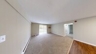 Located at 1 Lathrop Ln in Rocky Hill, Connecticut, this two-bedroom, one-bathroom residence offers a functional and comfortable single-floor layout. The expansive living room serves as the heart of the home, featuring wall-to-wall carpeting, baseboard heating, a wall-mounted air conditioning unit, and a sliding glass door with vertical blinds that fills the space with natural light and provides views of the surrounding greenery. A hardwood-floored entryway transitions seamlessly into the carpeted living areas. The two bedrooms are well-proportioned, each offering plush carpeting, baseboard heating, and generous sliding-door closets. The primary bedroom is notably spacious, with dual windows that bring in abundant natural light and outdoor views. The second bedroom also benefits from natural light and a large closet. A connecting hallway with three closets provides ample storage throughout. The full bathroom is finished with clean white fixtures, a tub-shower combination, a single-sink vanity, and warm wood-tone flooring. The neutral, warm beige tones throughout the residence create a cohesive and understated aesthetic, offering a move-in-ready canvas adaptable to any décor style.