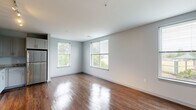 Located at 107 S River Rd in Bedford, NH, this well-appointed 2-bedroom, 2-bathroom residence offers a thoughtfully designed single-level layout. Rich hardwood flooring flows through the open-concept living room and kitchen, reflecting natural light from multiple windows that frame views of surrounding greenery. The kitchen is outfitted with granite countertops, shaker-style cabinetry in a contemporary gray-and-white finish, stainless steel appliances including a refrigerator, range, microwave, and dishwasher, and track lighting overhead. The living area is bright and open, with large windows providing lush outdoor views. The spacious primary bedroom features gleaming hardwood floors and oversized windows that flood the room with natural light and treetop scenery. The second bedroom is finished with plush carpeting and its own window with outdoor views. Each bathroom is finished with granite-topped vanities and tile flooring; one includes a tub-shower combination with brushed gold fixtures, while the other offers a walk-in shower. A dedicated closet provides additional storage. The soft, neutral color palette and clean lines throughout lend the space a modern, cohesive ambiance.
