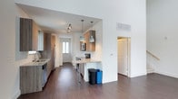 This two-story, 2-bedroom, 2-bathroom townhome offers a well-designed layout with contemporary finishes throughout. The kitchen is a standout feature, showcasing warm wood cabinetry, granite-look countertops, and a peninsula that provides additional prep space and casual seating. Stainless steel appliances, including a range, microwave, and refrigerator, are complemented by a white subway tile backsplash, lending a clean, modern aesthetic. Pendant lighting with industrial-style fixtures hangs above the peninsula, adding character and focused illumination. Rich, dark hardwood-style flooring runs throughout the main level, creating a cohesive and polished look. The open-concept flow connects the kitchen to the main living areas, enhancing the sense of space and functionality. A private entrance door at the rear of the kitchen is a defining townhome feature, offering direct access to the outdoors. Recessed and track lighting provides ample illumination throughout. The two-floor layout allows for a clear separation between living and sleeping areas, offering privacy and versatility. Overall, the space combines practical design with modern style, making it a well-appointed and comfortable home.