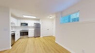 This thoughtfully designed 2-bedroom, 1-bathroom residence offers a functional and modern living experience across a single floor. The open living area is finished with light wood-style flooring and crisp white walls, illuminated by multiple windows fitted with slatted blinds that allow natural light to filter through. The kitchen is a standout feature, showcasing white shaker-style cabinetry, a classic subway tile backsplash, white quartz countertops, and a full suite of stainless steel appliances including a refrigerator, range, over-the-range microwave, and dishwasher. A double-door closet adjacent to the kitchen provides convenient additional storage. Both bedrooms are carpeted and feature neutral walls with windows that bring in natural light. The primary bedroom is generously sized and includes a ceiling fan with light fixture, while the second bedroom offers a quieter, more compact layout. The bathroom is neatly finished with large-format gray tile surrounding the tub-shower combination, brushed nickel fixtures, a white vanity, and wood-style flooring. A hallway and dedicated closet complete the layout, offering practical organization throughout this clean and move-in-ready residence.