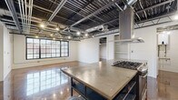 This Birmingham unit showcases a striking industrial aesthetic throughout its single-floor layout, accommodating three bedrooms, three bathrooms, and a dedicated utility room. The design is defined by soaring exposed ceilings with visible steel beams, ductwork, and track lighting, creating a raw, warehouse-inspired atmosphere complemented by polished, stained concrete floors that reflect light throughout the space.

The kitchen serves as a functional centerpiece, featuring a concrete-topped island with a gas range, a stainless steel refrigerator, open live-edge wood shelving, concrete perimeter countertops, and a prominent stainless steel range hood. The open-plan living area benefits from large, steel-framed grid windows that invite natural light and neighborhood views.

Each bedroom continues the industrial theme with exposed ceiling structures, shiplap accent walls, polished concrete floors, and black-framed windows providing natural light. Four closets offer practical storage throughout the unit.

The three bathrooms blend industrial and farmhouse elements, featuring white subway tile tub surrounds, shiplap walls, stained concrete floors, concrete vanity countertops with metal-framed storage below, and Edison bulb sconce lighting, creating a cohesive and well-detailed finish.