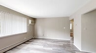 Located at 1800 Park West Blvd in Griffith, Indiana, this two-bedroom, one-bathroom single-floor unit offers a practical and comfortable layout with a clean, neutral aesthetic throughout. The living room is a generous open space finished with light gray luxury vinyl plank flooring, warm taupe walls, and a large window with vertical blinds that invites natural light. A wall-mounted air conditioning unit and baseboard heating ensure year-round comfort. The kitchen makes a bold statement with dark espresso cabinetry, light countertops, and black appliances including an electric range and refrigerator. A ceiling fan adds airflow, and a built-in shelved closet provides convenient pantry storage. Both bedrooms are carpeted in warm beige tones and feature natural light from windows with blinds and baseboard heating. The primary bedroom is notably spacious, offering dual reach-in closets with bifold doors and generous hanging and shelf space. The second bedroom is cozy and well-proportioned, with easy hallway access. The full bathroom features a clean white tub-shower combo with built-in shelving and chrome fixtures. A hallway connects all rooms, contributing to a cohesive and efficient floor plan throughout this well-appointed home.