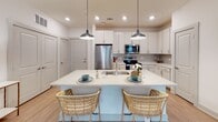 Located at 1001 Boopa Ln in Mount Pleasant, SC, this thoughtfully designed single-floor residence offers a bright, open layout with cohesive modern finishes throughout. The open-concept kitchen serves as a central hub, featuring crisp white cabinetry, a tile backsplash, stainless steel appliances including a full-size refrigerator, microwave, and range, and a generous island with a double sink and seating for two — illuminated by stylish pendant lighting. Light wood-style flooring extends seamlessly from the kitchen into the living area, which is filled with natural light from large windows framed by floor-length curtains and equipped with a ceiling fan. The primary bedroom is a serene retreat with plush carpeting, a ceiling fan, and direct access to an en-suite bathroom featuring a double vanity and a glass-enclosed walk-in shower. A second bathroom offers a single vanity and shower-tub combination. A versatile flex room with a ceiling fan and large window provides an ideal space for a home office or additional bedroom. Clean white walls, recessed lighting, and a consistent neutral palette give the entire residence a polished, contemporary feel.