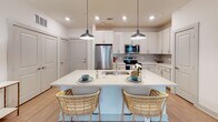 Located at 1001 Boopa Ln in Mount Pleasant, SC, this thoughtfully designed single-floor residence offers a bright, open layout with cohesive modern finishes throughout. The open-concept kitchen serves as a central hub, featuring crisp white cabinetry, a tile backsplash, stainless steel appliances including a full-size refrigerator, microwave, and range, and a generous island with a double sink and seating for two — illuminated by stylish pendant lighting. Light wood-style flooring extends seamlessly from the kitchen into the living area, which is filled with natural light from large windows framed by floor-length curtains and equipped with a ceiling fan. The primary bedroom is a serene retreat with plush carpeting, a ceiling fan, and direct access to an en-suite bathroom featuring a double vanity and a glass-enclosed walk-in shower. A second bathroom offers a single vanity and shower-tub combination. A versatile flex room with a ceiling fan and large window provides an ideal space for a home office or additional bedroom. Clean white walls, recessed lighting, and a consistent neutral palette give the entire residence a polished, contemporary feel.