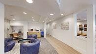 Located at 800 Victors Way in Ann Arbor, Michigan, this single-floor space offers a well-appointed layout that seamlessly blends professional functionality with a welcoming, residential-inspired atmosphere. Light hardwood flooring flows throughout, unifying the distinct zones within the space.

The expansive living room serves as the heart of the layout, offering multiple seating configurations. A central lounge area features rounded, upholstered chairs arranged around a coffee table on a patterned area rug, anchored beneath a curved ceiling detail with recessed lighting. Bold houndstooth-patterned accent walls add a dynamic visual element, while a built-in refreshment station with a beverage cooler and cabinetry provides added convenience. A separate seating nook showcases a teal accent wall adorned with sculptural wall art, a plush sofa, and a low-profile coffee table. Natural light filters in through windows dressed with sheer curtains, and framed botanical artwork decorates the walls alongside a wall-mounted television.

The private office is efficiently arranged with an L-shaped wood-finish desk, dual monitors, and a window with slatted blinds that allows for natural light while maintaining privacy. The grey textured accent wall lends a clean, modern backdrop to the workspace. Together, these areas create a polished, inviting environment suited for both client engagement and day-to-day operations.
