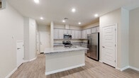 This two-story home offers a thoughtfully designed layout with modern finishes throughout. The kitchen serves as a central highlight, showcasing grey shaker-style cabinetry, granite countertops, and a full suite of stainless steel appliances including a range, built-in microwave, and French door refrigerator. A central island with a granite surface and undermount sink provides additional workspace and casual seating. Light wood-style flooring runs throughout the main level, complementing the neutral warm-toned walls and recessed lighting overhead. A convenient half-bath on the main floor features a pedestal sink and an oval mirror, offering a clean and minimal aesthetic. The dedicated laundry room houses a full-size washer and dryer. Upstairs, the carpeted bedrooms are generously proportioned, each equipped with ceiling fans and windows that invite natural light. The primary bedroom connects to a full bathroom featuring a dual-sink vanity with granite countertops, grey cabinetry, and a shower-tub combination. A spacious walk-in closet with multi-tier shelving and hanging rods provides ample storage. The overall design is clean, contemporary, and move-in ready.