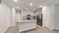 This two-story home offers a thoughtfully designed layout with modern finishes throughout. The kitchen serves as a central highlight, showcasing grey shaker-style cabinetry, granite countertops, and a full suite of stainless steel appliances including a range, built-in microwave, and French door refrigerator. A central island with a granite surface and undermount sink provides additional workspace and casual seating. Light wood-style flooring runs throughout the main level, complementing the neutral warm-toned walls and recessed lighting overhead. A convenient half-bath on the main floor features a pedestal sink and an oval mirror, offering a clean and minimal aesthetic. The dedicated laundry room houses a full-size washer and dryer. Upstairs, the carpeted bedrooms are generously proportioned, each equipped with ceiling fans and windows that invite natural light. The primary bedroom connects to a full bathroom featuring a dual-sink vanity with granite countertops, grey cabinetry, and a shower-tub combination. A spacious walk-in closet with multi-tier shelving and hanging rods provides ample storage. The overall design is clean, contemporary, and move-in ready.