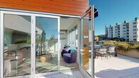Located at 1363 Colton Street in the Echo Park neighborhood of Los Angeles, this contemporary rooftop amenity space seamlessly blends indoor comfort with outdoor living. The building's exterior showcases a striking combination of warm wood cladding and clean white stucco, giving it a modern, design-forward aesthetic.

The interior lounge area features light hardwood flooring, crisp white walls, and an abundance of natural light streaming through expansive floor-to-ceiling glass sliding doors. Plush, rounded purple lounge chairs with teal accent pillows create a comfortable and inviting seating arrangement, complemented by a round side table. A wall-mounted mini-split system ensures climate comfort, and an "INSPIRE" sign adds a casual, community-oriented touch to the space.

Large glass panel doors open directly onto a spacious outdoor terrace, where residents can enjoy the Southern California sunshine. The terrace is well-appointed with bar-height seating, patio tables, and shade umbrellas, all set against a backdrop of sweeping urban views of the Los Angeles skyline and surrounding Echo Park neighborhood. Ornamental grasses in raised white planters add a touch of greenery to the rooftop setting, enhancing the overall atmosphere of this vibrant communal space.