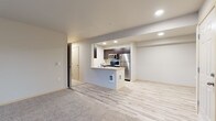 This single-floor residence offers a clean, contemporary design with a thoughtful layout that balances open living spaces and private quarters. The heart of the unit is an open-concept kitchen and living area, where light wood-style flooring flows seamlessly beneath recessed lighting. The kitchen is equipped with stainless steel appliances—including a refrigerator, range, and built-in microwave—complemented by rich dark cabinetry and a peninsula counter that provides both workspace and a natural divide from the living area. The spacious living room transitions from hard flooring to plush carpet and features a sliding glass door that opens to a private balcony, inviting natural light and outdoor views into the space. The bedrooms are generously sized, finished with soft carpeting, and each features windows overlooking the surrounding neighborhood, filling the rooms with natural daylight. The bathroom is finished with light tile flooring and includes a wide vanity topped with a large mirror, sleek dark cabinetry with brushed hardware, and a separate toilet and tub area. Throughout the unit, neutral tones and consistent finishes create a cohesive, move-in-ready atmosphere that is both functional and inviting.