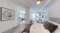 Located at 445 Hialeah Dr in Hialeah, FL, this thoughtfully designed single-floor residence offers a bright, contemporary living experience. The open-concept layout is defined by light wood-look flooring, crisp white walls, and ceiling fans throughout, creating an airy and cohesive atmosphere.

The living area is centered around a wall-mounted flat-screen TV and features a stylish open-grid wood shelving unit that serves as an elegant room divider, visually separating the sleeping and living spaces while maintaining an open, connected feel. Large windows invite generous natural light, enhancing the overall brightness of the space.

The kitchen is well-appointed with flat-front cabinetry in a warm gray tone, subway tile backsplash, white quartz-style countertops, and a full suite of stainless steel appliances including a side-by-side refrigerator, electric range, built-in microwave, and a single-basin sink. The dining area sits adjacent, accommodating a small table and chairs.

The bedroom is a tranquil retreat, complete with a ceiling fan, a walk-in closet, and seamless access to the rest of the unit. The bathroom features a modern vanity with a framed mirror, under-mount sink, and clean tile flooring, finishing the space with a refined, contemporary touch.