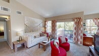 This single-floor residence offers a thoughtfully designed layout with a seamless flow between its main living spaces. The bright and spacious living room is anchored by vaulted ceilings and large sliding glass doors that open onto a private balcony, framing views of surrounding greenery. Patterned curtains and plush carpeting add warmth to the space, which connects naturally to a dedicated dining area illuminated by a statement chandelier and hardwood-style flooring.

The kitchen is well-equipped with rich warm-toned wood cabinetry, granite-style countertops, a gas range, microwave, and a full-size refrigerator. A generous breakfast bar provides additional prep and dining space, while multiple windows ensure ample natural light throughout.

The bedrooms are comfortably sized with vaulted ceilings, soft carpeting, and large windows overlooking wooded surroundings, creating a calm and restful atmosphere. The primary bedroom benefits from direct access to a full bathroom featuring a tub-shower combination with tile surround and a walk-in closet with wire shelving. An additional bathroom includes a wood-vanity with a large mirror and stylish lighting fixtures, complemented by hardwood-style flooring throughout the hallway.