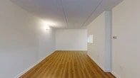 Located at 60 N De Baun Ave in Airmont, NY, this single-floor, two-bedroom, one-bathroom residence offers a practical and well-organized layout. Throughout the unit, warm wood-look laminate flooring runs continuously, complemented by crisp white walls, white baseboards, and textured ceilings that lend a clean, consistent aesthetic.

The combined living and dining room serves as the central gathering space, offering generous room for both lounging and dining. A wall sconce provides ambient lighting, and a pass-through window connects this area to the kitchen, enhancing the open feel. The kitchen features wooden cabinetry, a sink, and space for appliances, keeping functionality at the forefront.

Both bedrooms are well-proportioned, each equipped with baseboard heating and windows that invite natural light and outdoor views of surrounding greenery. The primary bedroom includes a double-door closet for ample storage, and additional closets — four in total throughout the unit — provide excellent organizational capacity.

The bathroom is finished with white tile flooring and includes a full tub and shower combination with a sliding door enclosure, a wood-toned vanity with an integrated sink, and a wall-mounted mirror. A hallway connects the main areas of the unit, contributing to a logical and efficient flow throughout the residence.