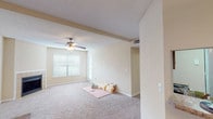 This single-floor, 2-bedroom, 2-bathroom residence offers a thoughtfully designed layout with a warm, neutral color palette throughout. The expansive living area features plush carpeting, a ceiling fan with light fixture, and a fireplace that serves as a focal point, complemented by natural light from multiple windows. Adjacent to the living space is a dining area, seamlessly connected to the kitchen via a pass-through window. The kitchen is well-appointed with rich oak cabinetry, granite-style countertops, hardwood flooring, and black appliances, providing ample storage and prep space. Both bedrooms are generously sized with soft carpeting, ceiling fans, and windows that invite natural light. The two bathrooms are finished with granite-style countertops, large mirrors, and combination tub-shower units, with hardwood flooring adding a clean, polished look. Closet space is plentiful, with louvered bifold doors visible in the living area. Textured ceilings are consistent throughout the home, adding a classic touch. The overall layout, as seen in the dollhouse view, is efficiently organized and offers a comfortable, functional living environment.