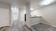 This single-story residence offers a practical and modern layout across two bedrooms and two bathrooms. The open-concept living and kitchen area serves as the heart of the unit, where a peninsula-style counter with a built-in sink and white upper cabinetry creates a natural divider between the kitchen and living space. A black range and overhead microwave complete the kitchen, while the pass-through counter design encourages an inclusive, connected atmosphere.

The living area features wood-style plank flooring in a neutral gray-tone finish, consistent throughout the entire unit, and is equipped with a ceiling fan. A built-in shelving nook adds a functional and decorative element to the living space. A hallway connects the living area to the two bedrooms and bathrooms.

The primary bedroom is generously sized, featuring a ceiling fan, a window allowing natural light, and a door leading to an en-suite bathroom. The second bedroom mirrors the same clean design, also including a ceiling fan and natural light. Each bathroom is finished with matching wood-style flooring and includes a full tub-shower combination. Neutral gray walls and white trim tie the entire unit together in a cohesive, contemporary aesthetic.